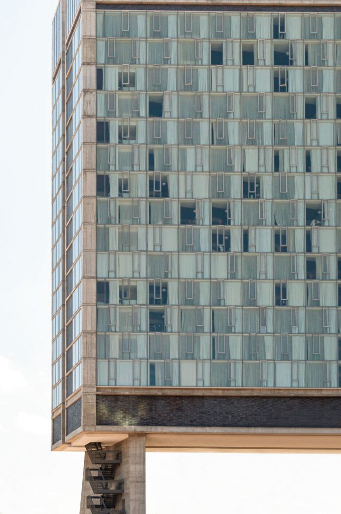 Tower of blue glass grid raised on pillars, shot frontally