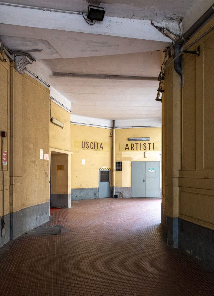 Theatre corridor with yellow walls and the illuminated signs USCITA and ARTISTI