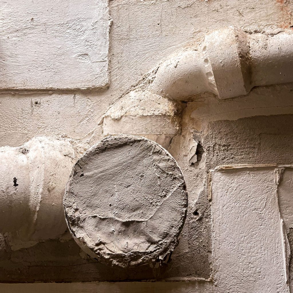 Detail of a rendered wall with a pipe and a round concrete disc