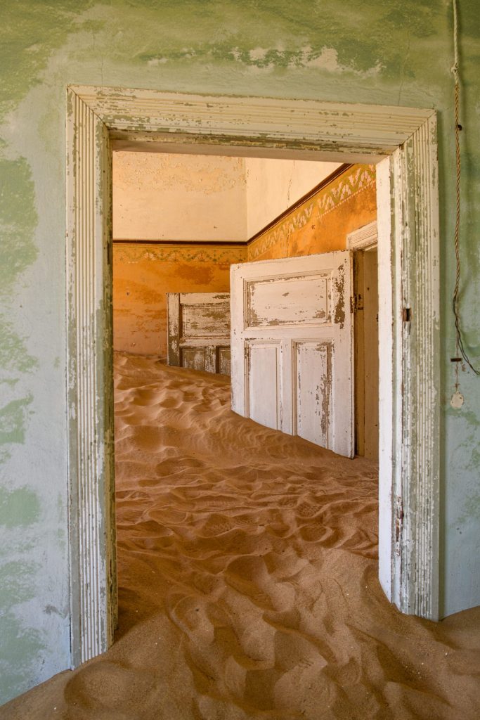 Abandoned room, a green door frame opening onto an ochre room with sand covering the floor