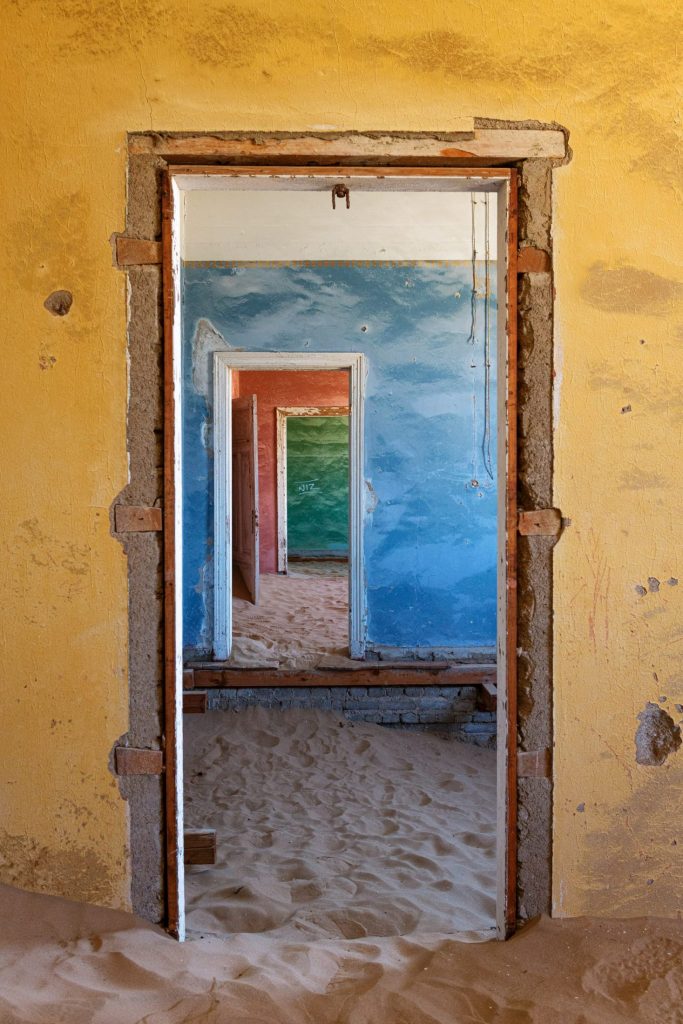 Yellow room with doors framing a succession of blue spaces, sand on the floor