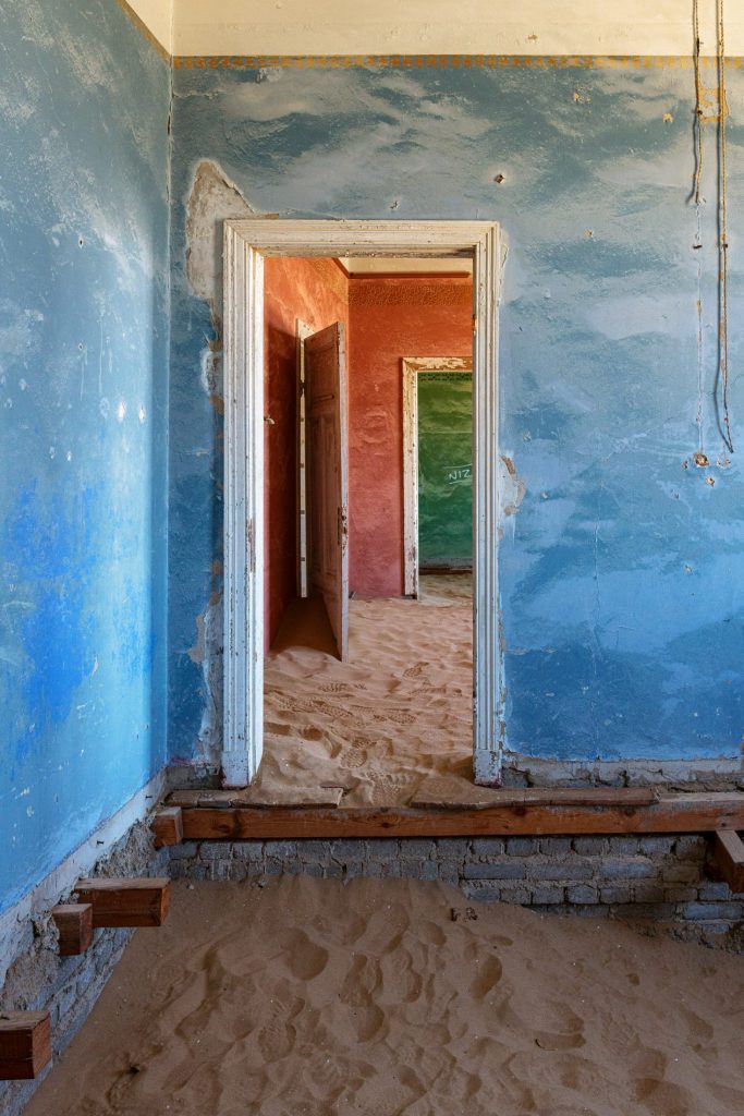 Blue room with a row of open doors and sand drifted across the floor