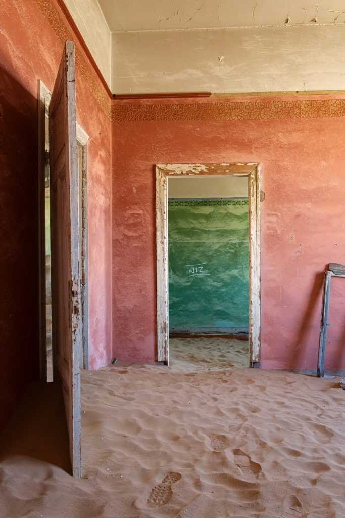 Room with pink and red walls and a green door, the floor covered in sand