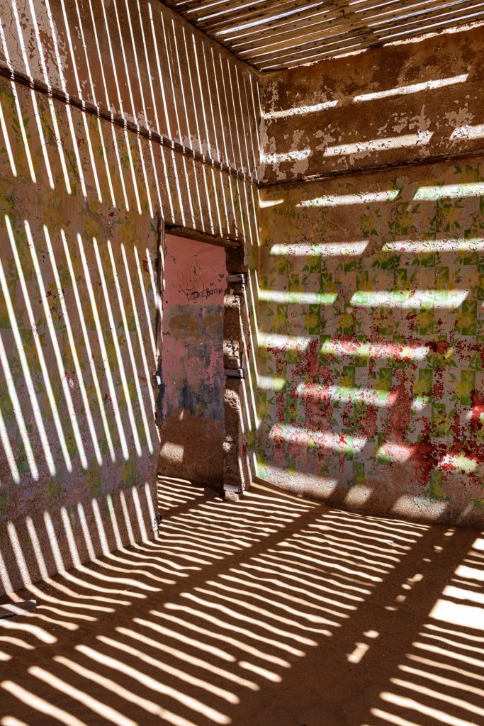 Room with blades of light cast by wooden slats across a wall bearing red graffiti