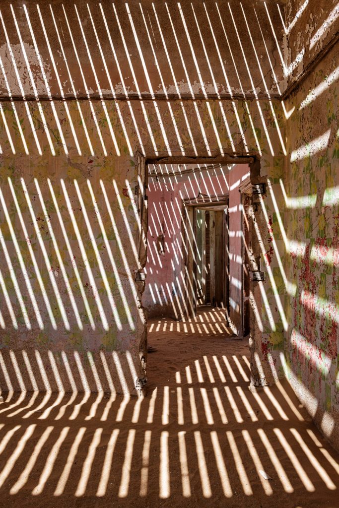 Stripes of light and shadow cast by wooden slats across the walls and floor of a room
