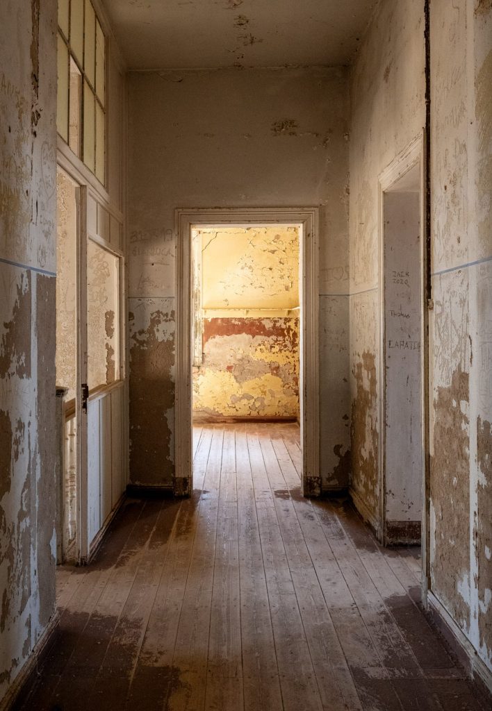 Corridor with a row of open doors, peeling walls and a pale wooden floor
