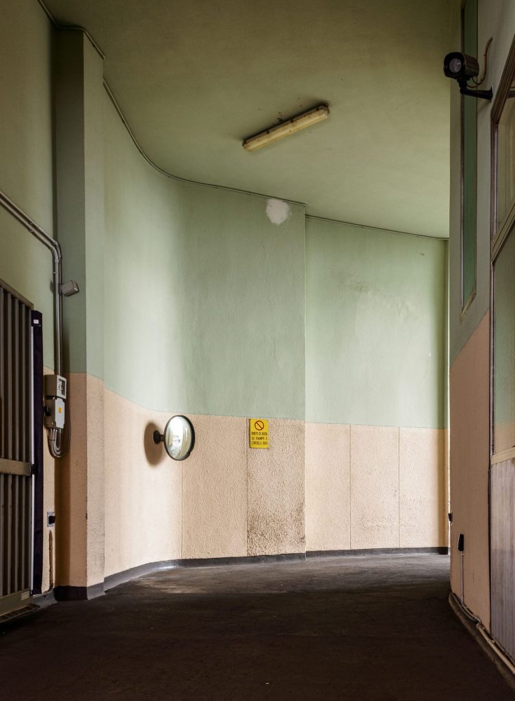 Garage corridor with pale green walls and a pink dado, a fluorescent tube overhead and a convex mirror