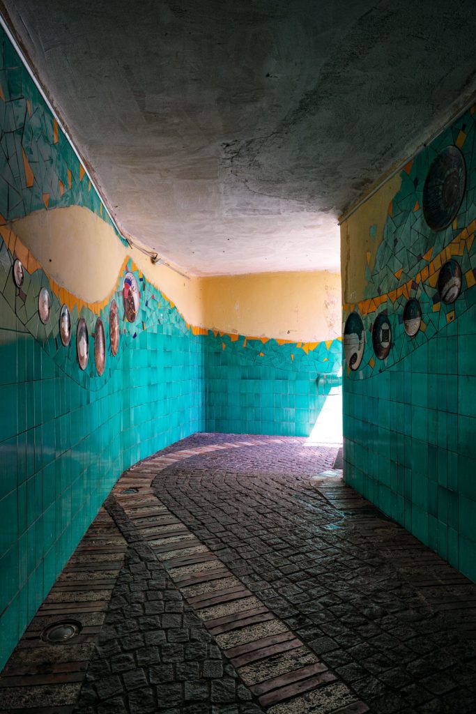 Vaulted corridor lined with turquoise majolica, terracotta floor, light entering from the far end