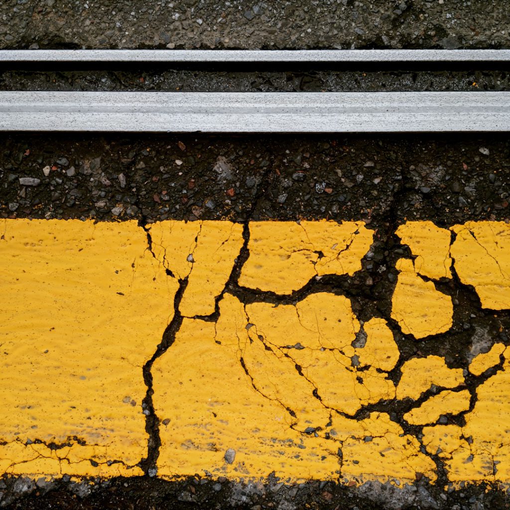 Cracked yellow asphalt beside a band of grey concrete