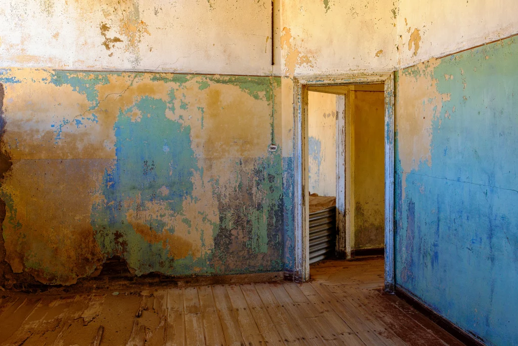 Room with peeling blue and ochre walls and a doorway on the right