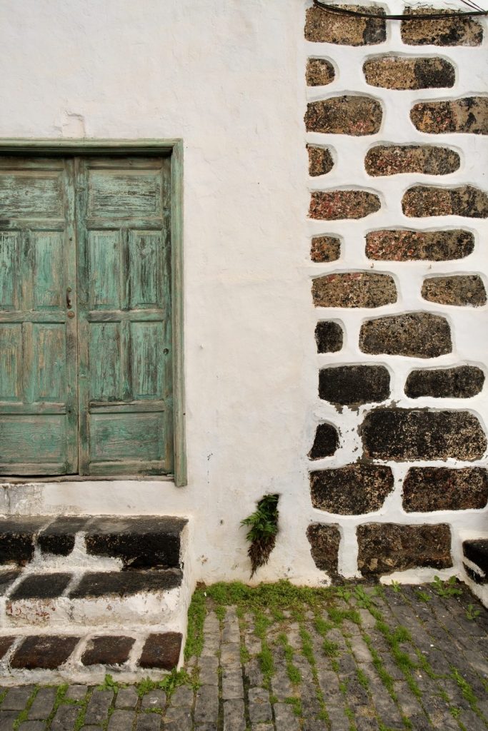 Weathered green wooden door set in a wall of stone and white lime render