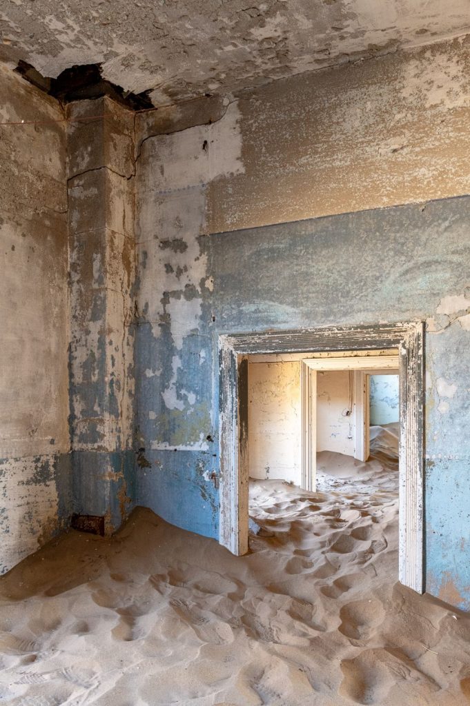 Abandoned room with peeling pale blue walls and sand drifting across the floor