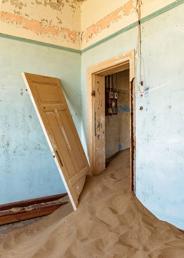 Detached door leaf leaning across a blue room invaded by sand