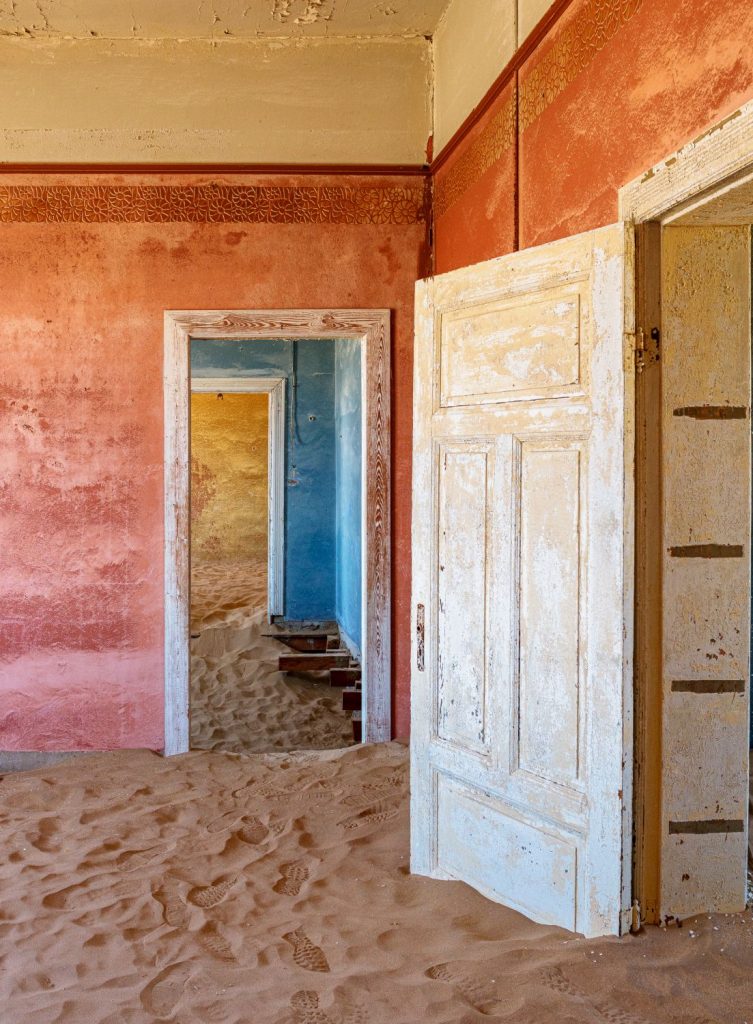 Room with pink walls, a white door ajar and sand on the floor