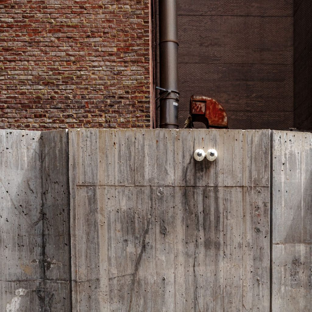 Concrete wall with a red pipe, exposed brickwork and two electrical sockets