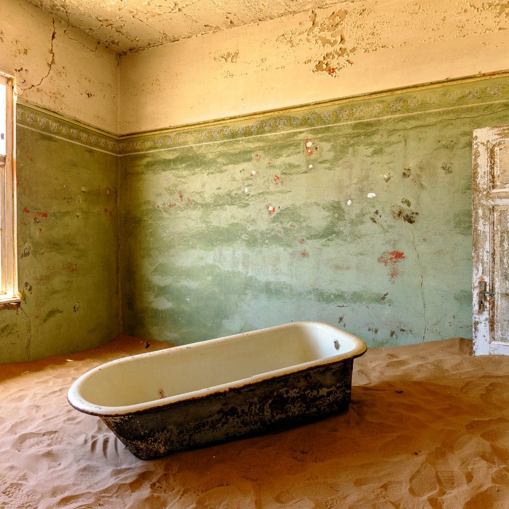 Room with green walls, an enamelled bathtub and sand on the floor