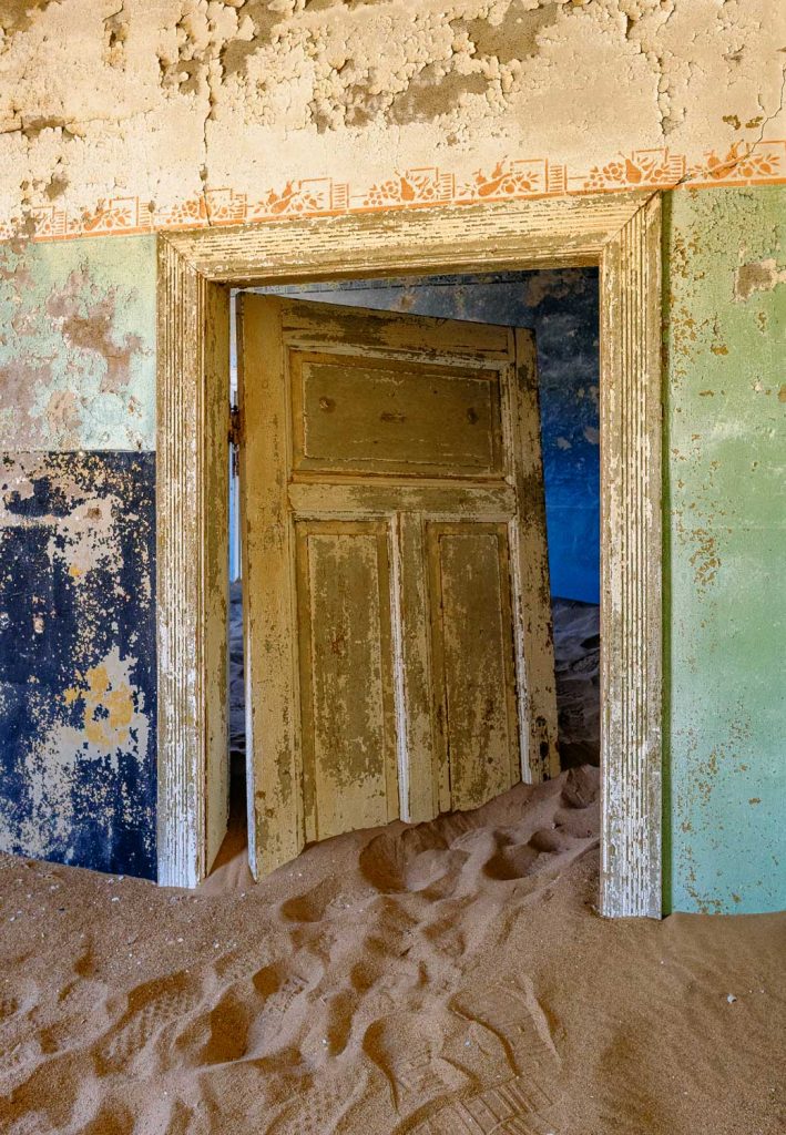 Peeling blue wooden door set in an ochre wall, sand on the floor