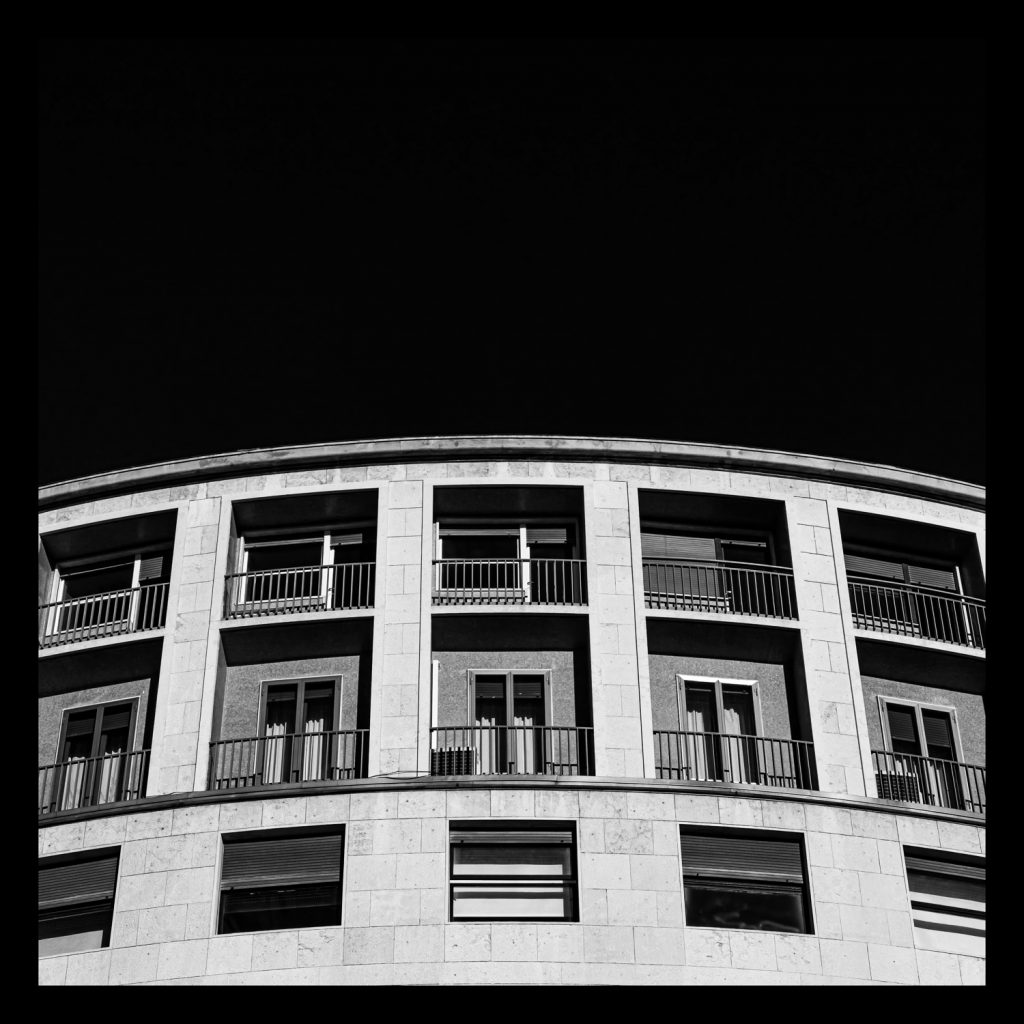 Corner building with a curved facade, in black and white against a black ground